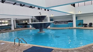 Una piscina interior con una fuente central, rodeada de sillones de descanso y un solárium con baldosas.