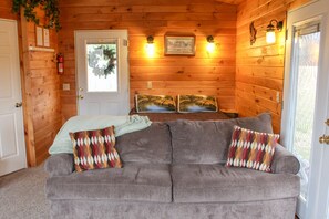 A cozy room with a gray sofa, two patterned pillows, a framed picture on the wall, and a door with a glass panel.