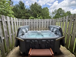 A hot tub with two side doors, a wooden deck, and a wooden fence in the background.