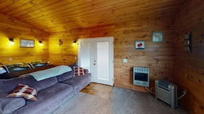 Ein gemütliches Blockhaus-Interieur mit Holzbalkendecke, einer Couch mit gemusterten Kissen, einer Tür mit Fenster und einem an der Wand befestigten Heizkörper.