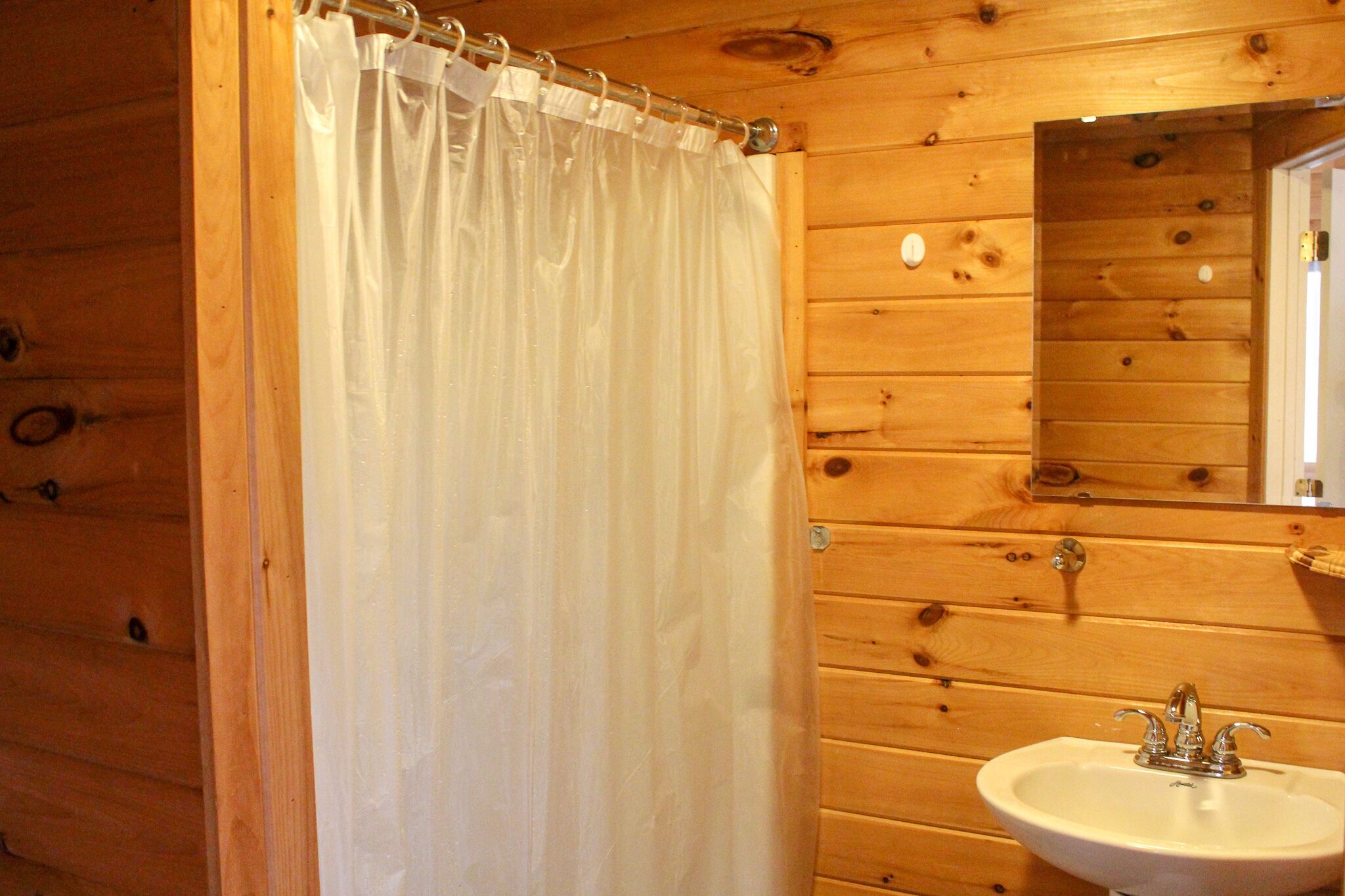 Un baño rústico con cabina de ducha de cortina blanca, lavamanos y espejo.