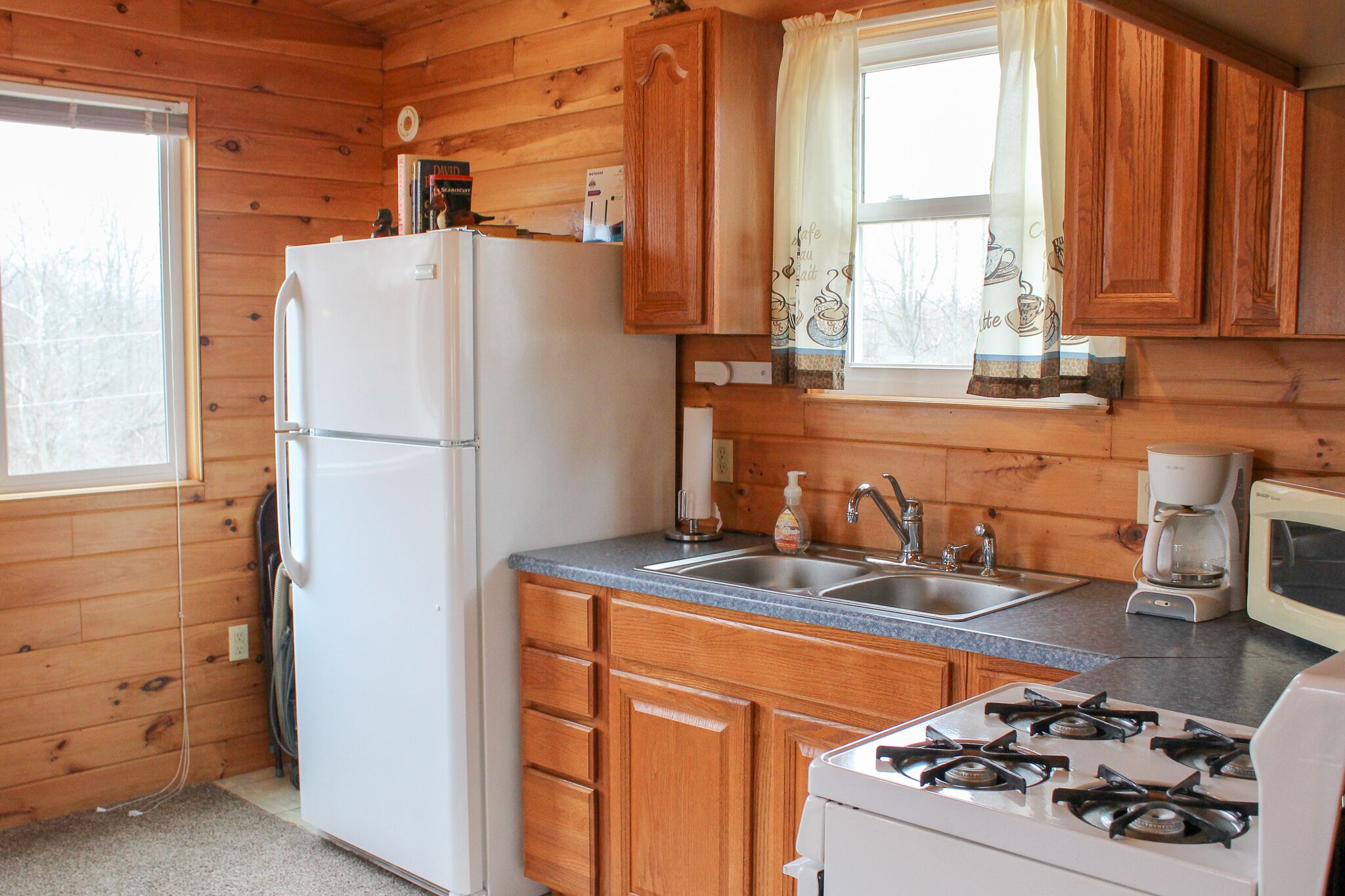 A compact kitchen with wooden cabinets, a refrigerator, a sink, a stove, and a microwave.