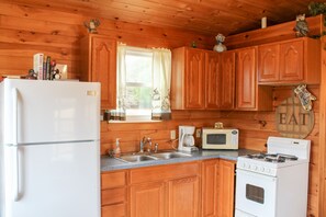A wooden cabin kitchen with a refrigerator, microwave, stove, sink, and wooden cabinets.