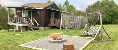 Eine Hütte mit Veranda, Schaukel und Feuerstelle im Garten.