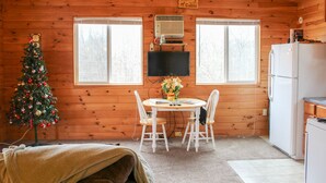 Interior acogedor de una cabaña con detalles de madera, una mesa de comedor con sillas, un árbol de Navidad, un televisor y un refrigerador.