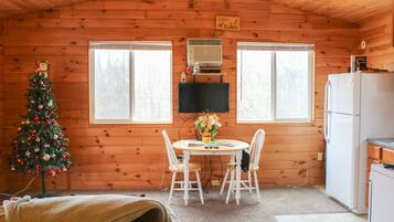L’intérieur chaleureux d’un chalet, avec un décor en bois, une table à manger et des chaises, un sapin de Noël, un téléviseur et un réfrigérateur.