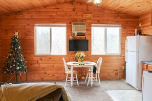 Ein gemütliches Blockhaus-Interieur mit Holzausstattung, einem Weihnachtsbaum, einem Esstisch mit Stühlen, einem Fernseher und einem Kühlschrank.