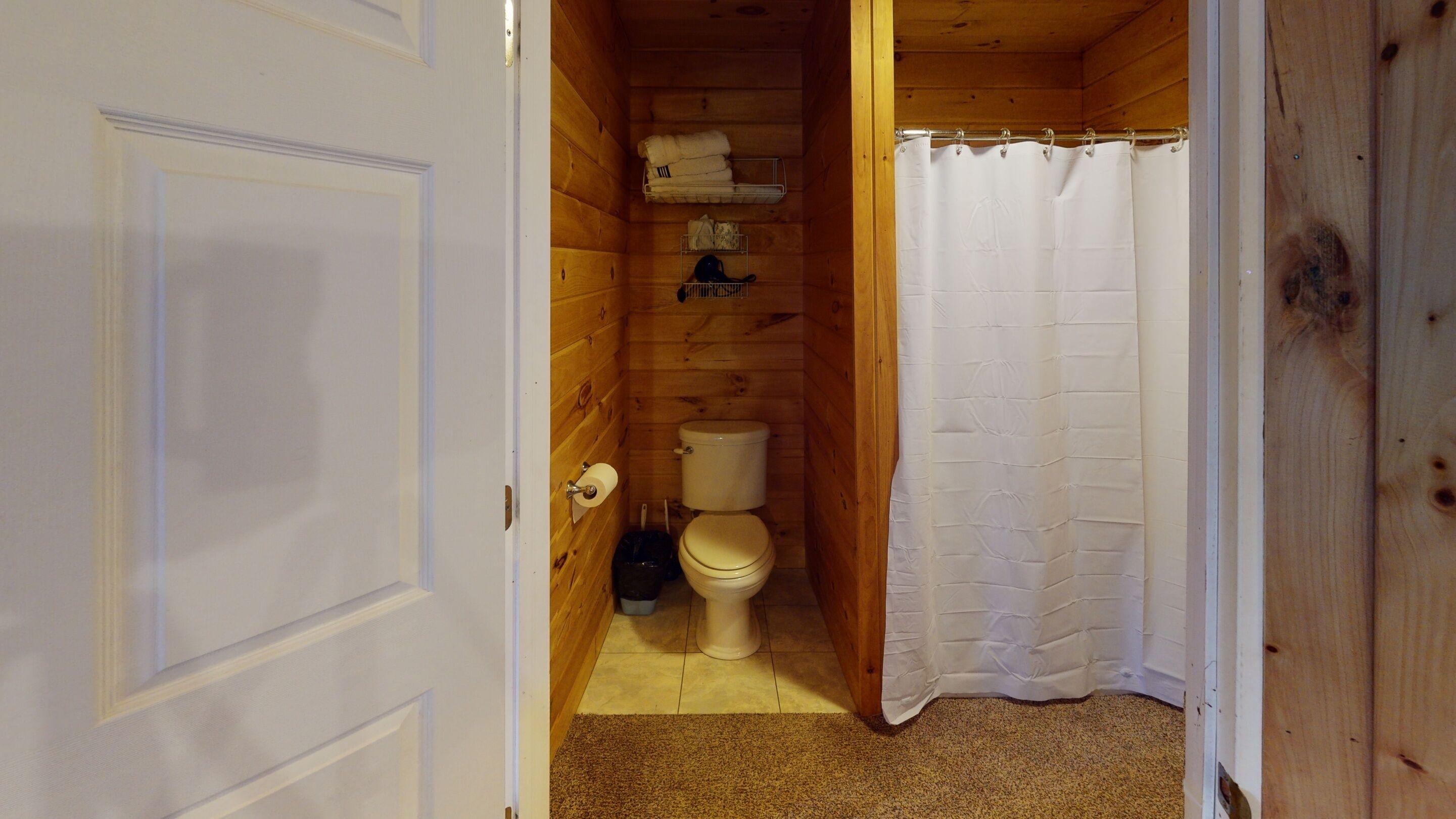 A small, wooden-paneled bathroom with a toilet, a shelf with towels, and a shower curtain.