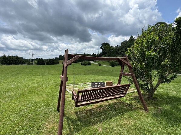 A wooden swing set in a grassy field with a bench and a bag labeled "LUDGING". - Cozy Hocking Hills Couples Cabin | Private Hot Tub (Nelsonville)