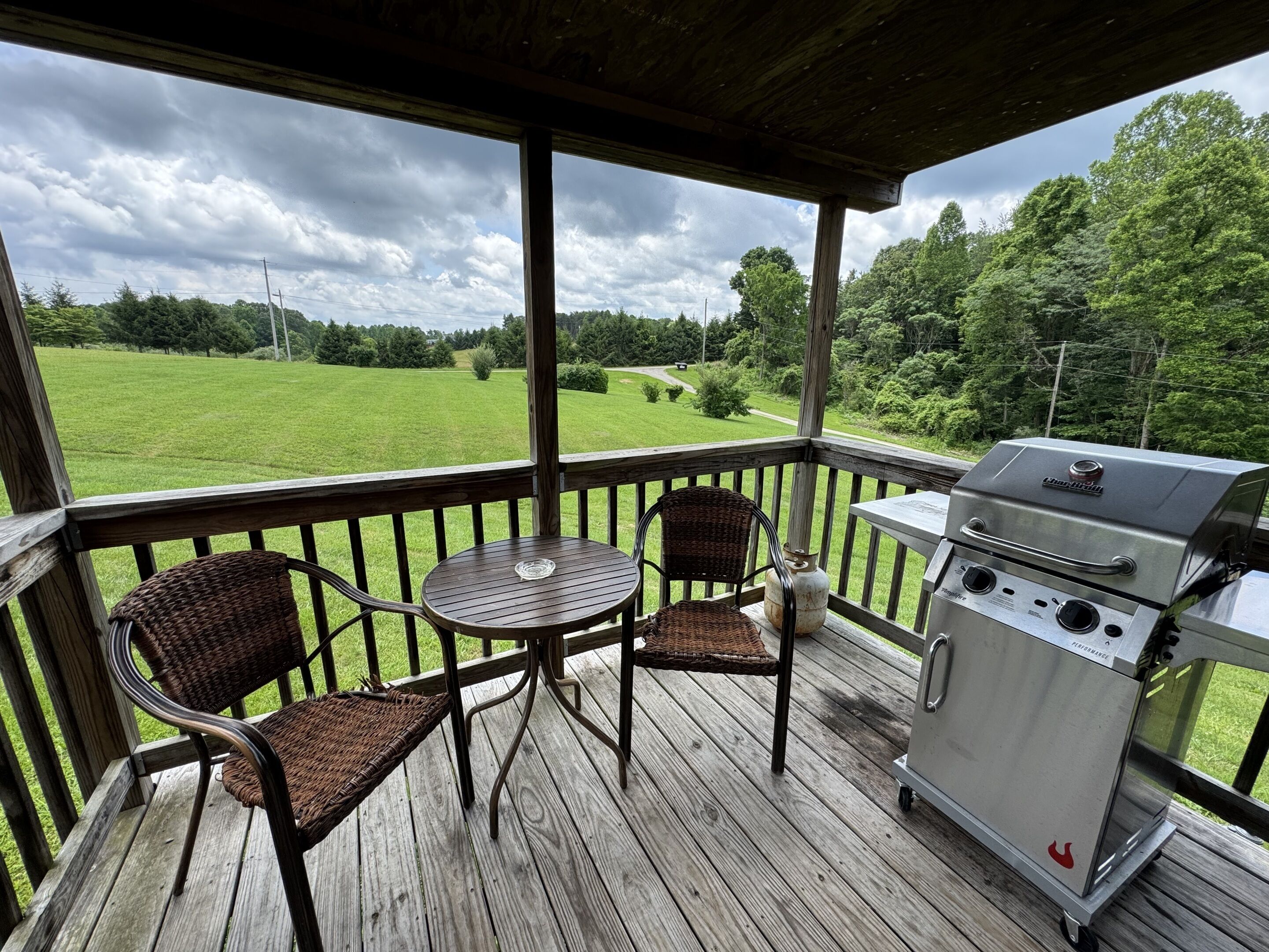 A covered outdoor area with a grill, wicker chairs, and a table.