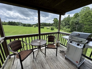 A covered outdoor area with a grill, wicker chairs, and a table.