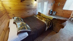 A wooden-paneled room with a bed, a small table, and a chair.