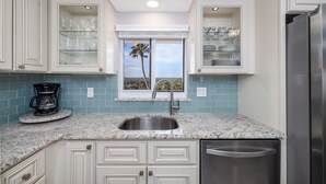 A kitchen with white cabinets, a stainless steel sink, and a view of the outdoors through a window. - Bring swim suit and start your beach holiday in this well appointed 2 bedroom 2 bath 3rd floor condo (New Smyrna Beach)