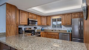 A kitchen with wooden cabinets, granite countertops, stainless steel appliances, and a window with blinds. - Centrally located ground floor two bedroom, walk right out to pools. (New Smyrna Beach)