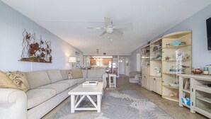 A spacious living room with a sofa, coffee table, and a decorative wall piece. - Centrally located ground floor two bedroom, walk right out to pools. (New Smyrna Beach)