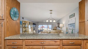 A kitchen with wooden cabinets, granite countertops, and a clock on the wall. - Centrally located ground floor two bedroom, walk right out to pools. (New Smyrna Beach)