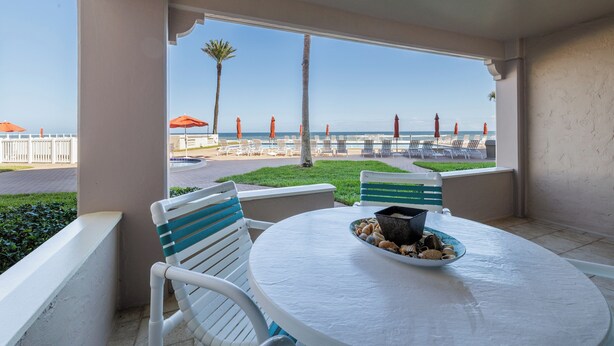 A balcony with a table, chairs, and a view of the beach. - Centrally located ground floor two bedroom, walk right out to pools. (New Smyrna Beach)