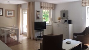 Een moderne woonkamer met een eethoek, een televisie op een meubel en een keuken met kasten en een aanrecht.