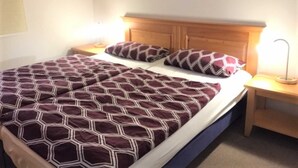 Een net opgemaakt bed met een sprei met een geometrisch patroon en passende kussens, een houten hoofdbord en twee bedlampen op nachtkastjes van hout.