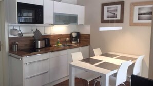 Een kleine keuken met witte kastjes, een magnetron, een koffiezetapparaat en een eethoek met een witte tafel en stoelen.
