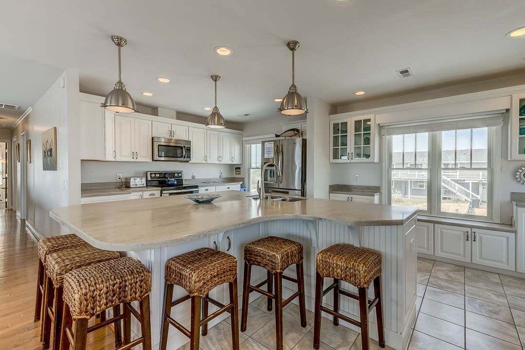 A spacious kitchen with white cabinets, stainless steel appliances, and a large island with bar stools.