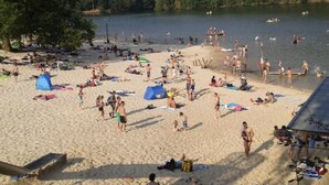 Ein voller Strand mit badenden Personen, Sonnenschirmen und Booten auf dem Wasser.