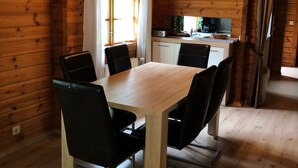 Ein Interieur einer Holzhütte mit einem Esstisch, Stühlen, einer Küchenzeile und einem Fenster mit Vorhängen.