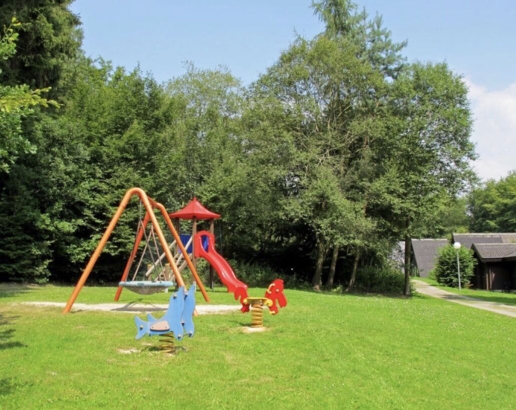 A playground with a swing set and a slide, surrounded by green grass and trees.