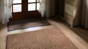 Ein Holzinnenraum mit einer Tür, die nach draußen führt, einem Holzkabinett und einer Fußmatte.