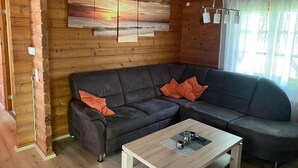 Ein gemütliches Cabin-Interieur mit einem dunkelgrauen Ecksofa, einem Holztisch und einem großen Gemälde einer untergehenden Sonne an der Wand.