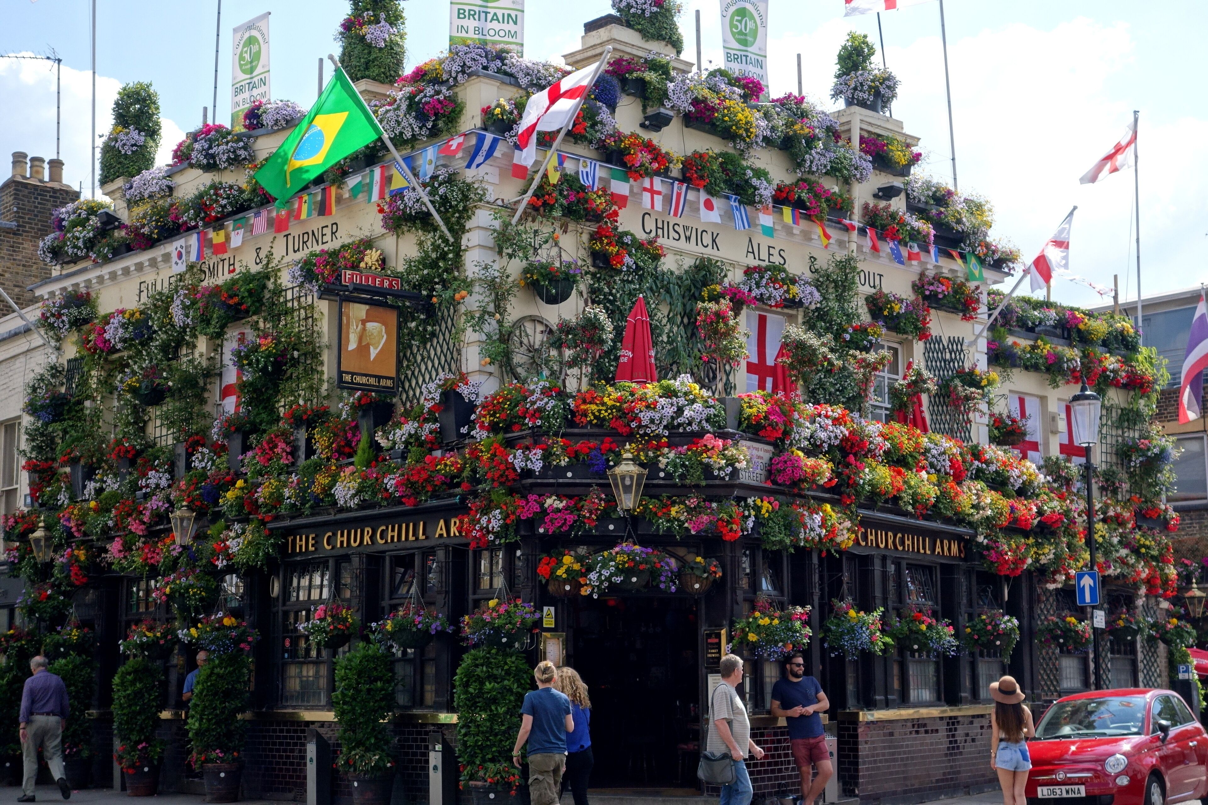 A pub with a traditional black facade, adorned with numerous flower baskets and flags.