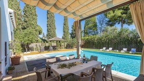 A poolside area with a covered patio, lounge chairs, and a table set for dining. - La Teja Holiday Home (Marchena)