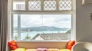 A window seat with cushions and a white chair, overlooking a body of water and distant hills.