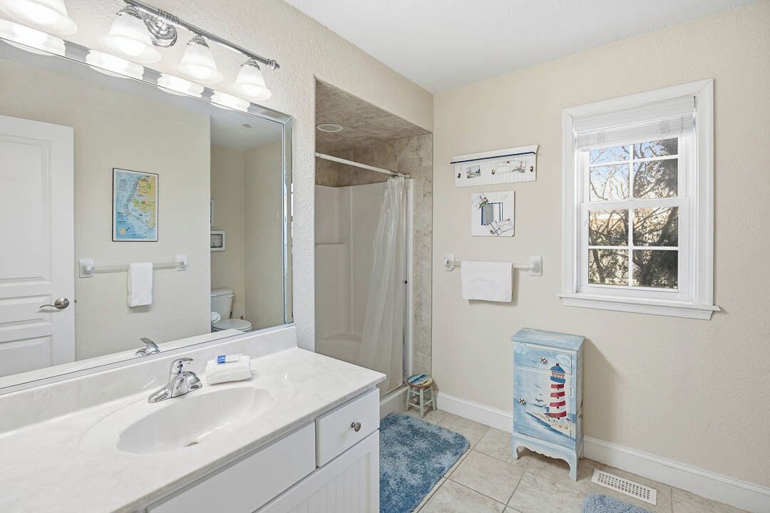 A bathroom with a white sink, mirror, and shower. There is a small stool and a blue cabinet with a lighthouse design.