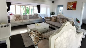 Un salon avec un canapé blanc, un canapé à motifs, une table basse blanche et un fauteuil blanc. Il y a un tableau au mur et une fenêtre avec des rideaux.