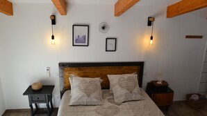 Ein Schlafzimmer mit hölzernem Kopfteil, zwei Nachttischen, einem Bett mit herzerstickter Bettwäsche, Wandleuchten und gerahmten Bildern.