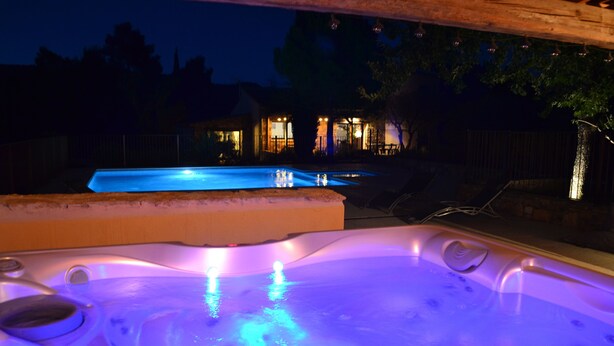 Ein Whirlpool mit blau beleuchtetem Innenraum, ein Schwimmbecken und eine Holzterrasse.