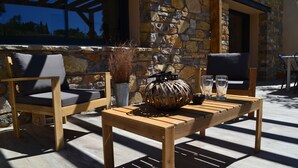 Eine Terrasse im Freien mit einem Holztisch, zwei Stühlen, einer Vase mit Trockenpflanzen und einem Glas Wasser.