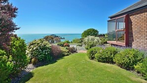 Una casa con vista al mar, un jardín con diversas plantas y fachada de ladrillo rojo.