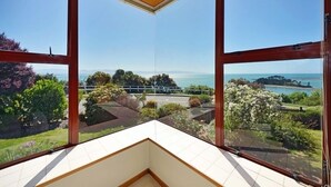 Una habitación con ventanas amplias que ofrecen vista a un jardín ajardinado y al mar.