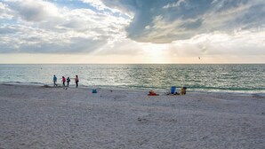 A beach with people walking and sitting on the sand, and a sunset in the background.