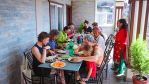 Eine Gruppe von Personen speist an einem Tisch, im Hintergrund eine Ziegelwand und große Fenster.