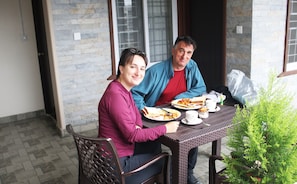 Two people sitting at a table with plates of food, a small plant, and a window in the background. - pokhara tourist home (Pokhara)