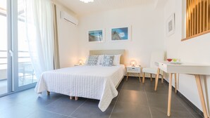 A modern bedroom with a large bed, bedside tables with lamps, a small desk, and a view through a sliding glass door. - Rotunda Suites (Chania)