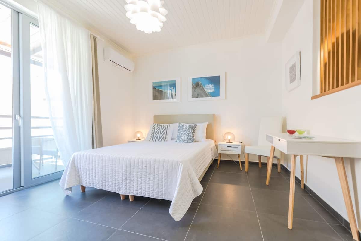 Une chambre moderne avec un grand lit, des tables de chevet avec des lampes, un petit bureau et une vue sur l’extérieur grâce à une porte-fenêtre coulissante.