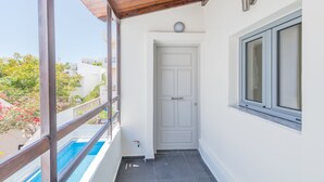 A balcony with a wooden railing, a white door, and a window with a view of buildings and trees. - Rotunda Suites (Chania)