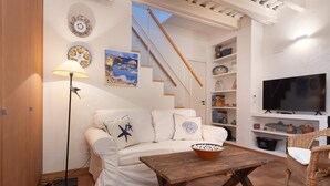 Una sala de estar con un sofá, una mesa de centro, un televisor, una lámpara y una escalera.
