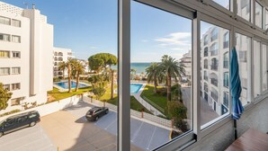 A hotel room with a large window overlooking a pool area, palm trees, and a building with balconies.