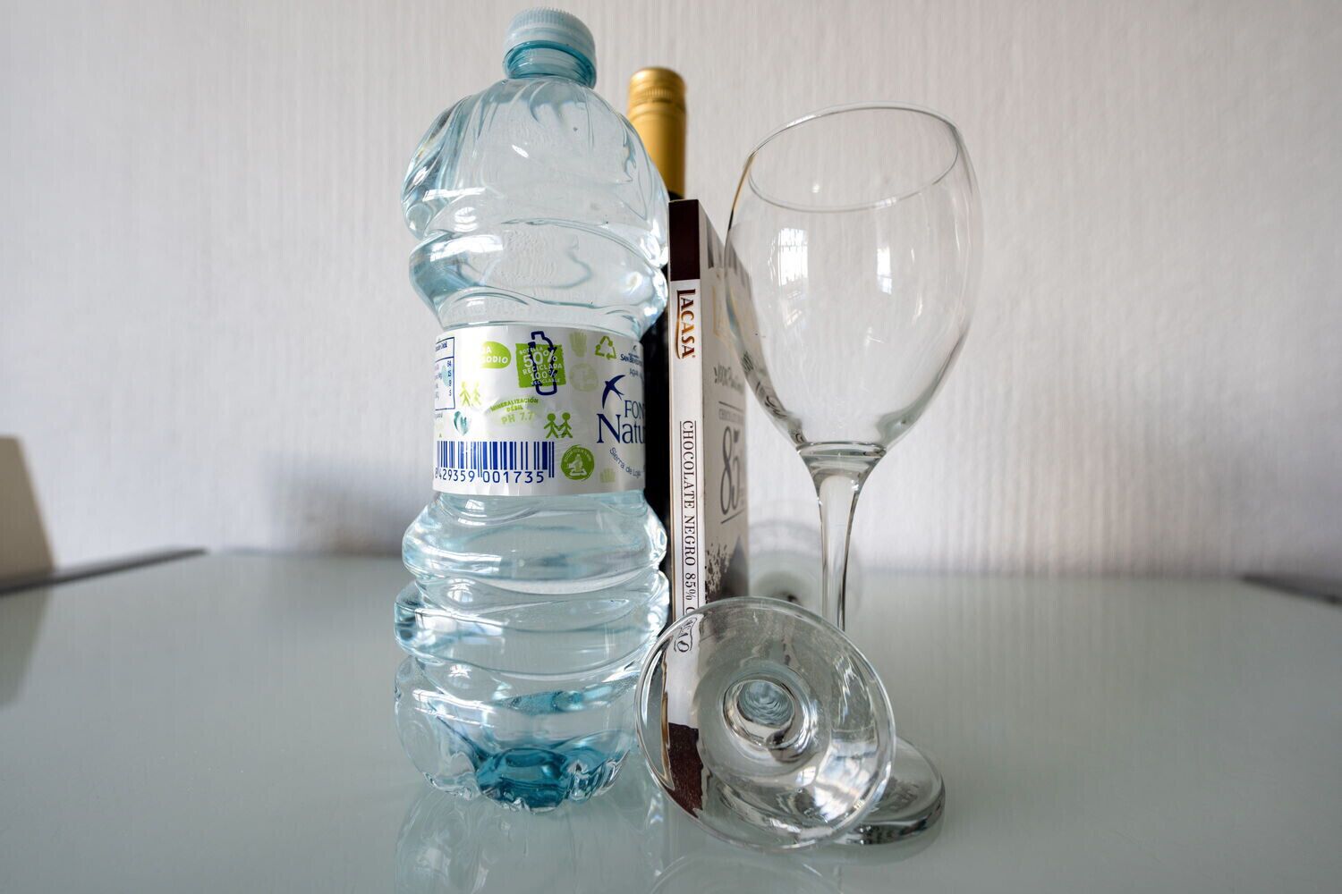 A clear glass bottle of water, a wine glass, and a book on a reflective surface.