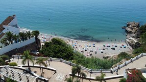 A beach with umbrellas and people, a rocky coastline, and a building with a white facade.